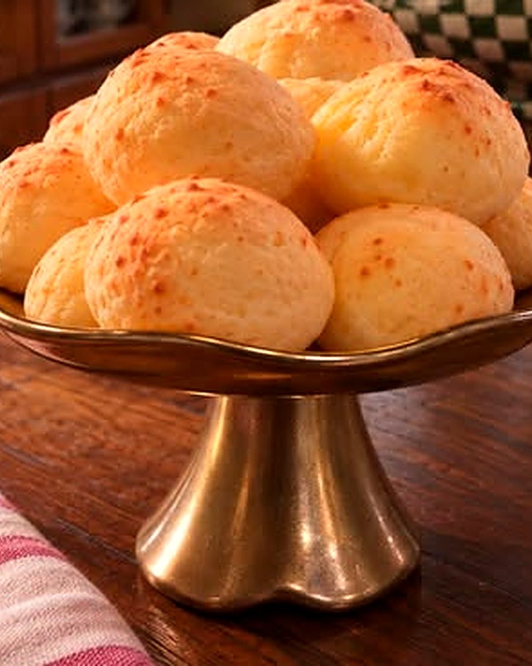 Pães de queijo dourados em uma boleira de cobre sobre mesa de madeira